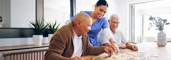 Two elderly men doing a puzzle with a support worker. 