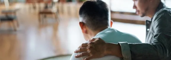 Someone putting their hand on another persons back in emotional support. 