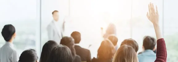 A group of people in a training session, one person has raised their hand to answer or ask a question.