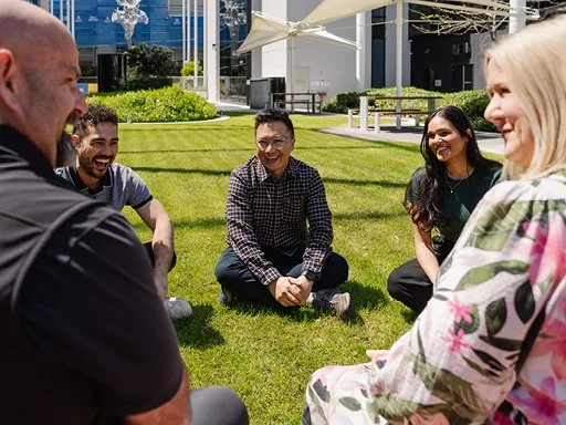 Group of people sitting on grass outside laughing and chatting. 