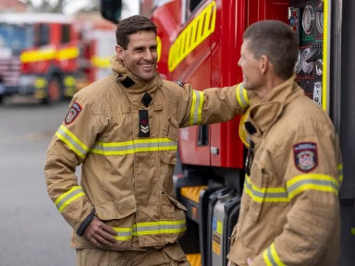 Two firefirefighters standing next to a firetruck.