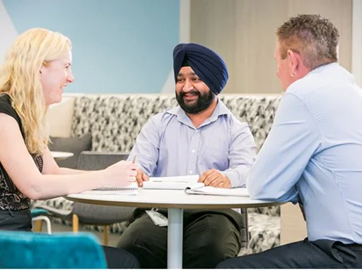 A group of three staff having a casual meeting around a table.