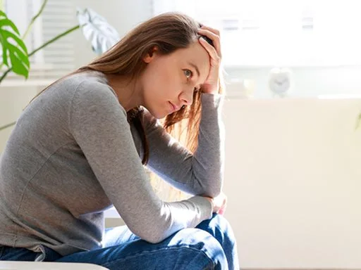 A young women sitting with head in hands looking tired and concerned. 