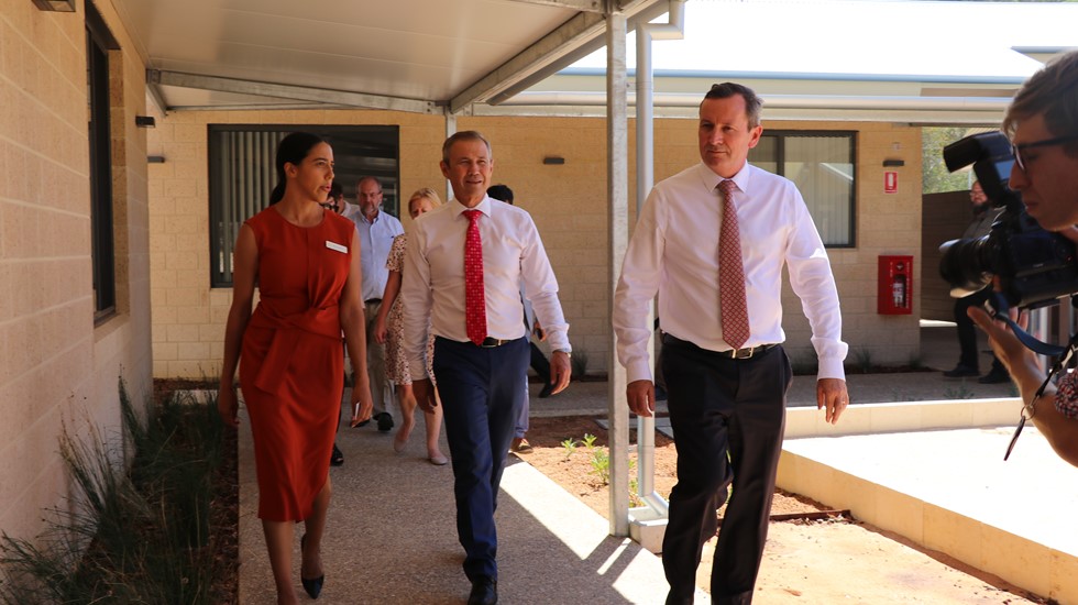 People walking along a shaded walkway outside a brick building