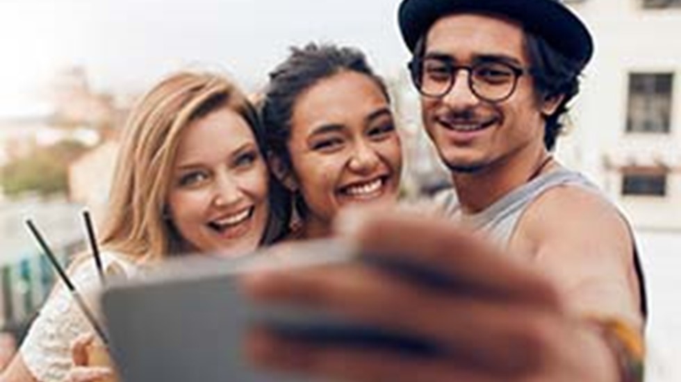 Three people stand close together, holding a phone for a selfie or a video call.