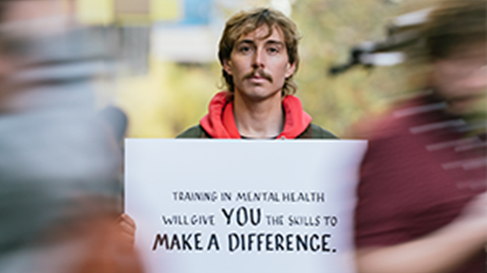 Young man holding a sign that reads: Training in mental health will give you the skills to make a difference.